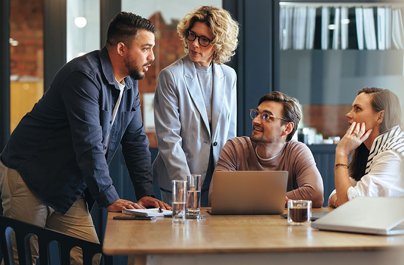 Man leaning on a desk while talking to colleagues